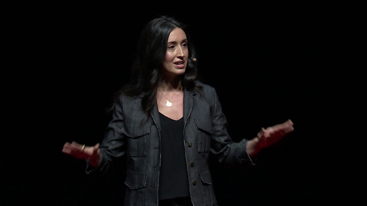 Erica Orange gesturing to audience with a mic in the TEDxBYU 2018 conference.